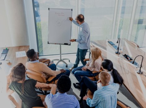 A photo of a man gesturing toward a white board for a small audience